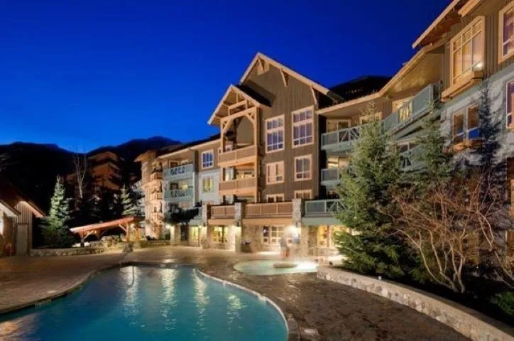 Pool at night featuring a community pool, a hot tub, and a patio area