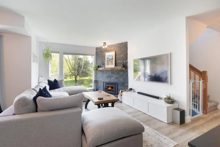 Living room with light wood-type flooring, a stone fireplace, and stairway