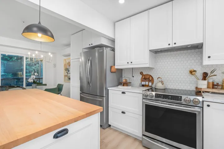 Kitchen featuring appliances with stainless steel finishes, white cabinets, decorative backsplash, decorative light fixtures, and wooden counters