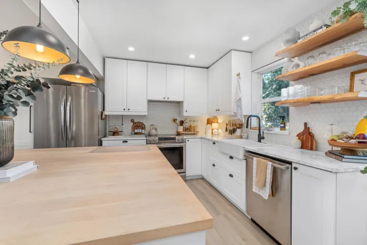 Kitchen with open shelves, backsplash, stainless steel appliances, white cabinetry, and hanging light fixtures