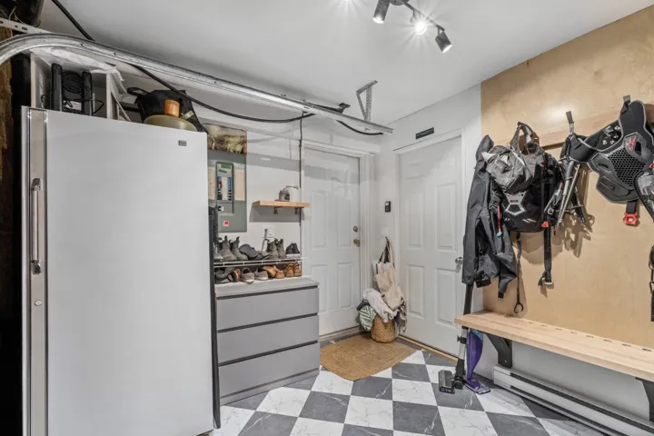 Below grade area featuring freestanding refrigerator, a baseboard heating unit, electric panel, and light flooring