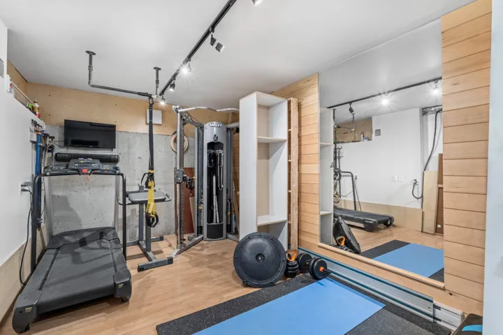 Exercise room with rail lighting, light wood-style floors, and wood walls