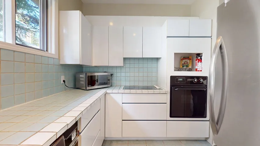 Kitchen with black appliances, white cabinetry, tile counters, and tasteful backsplash