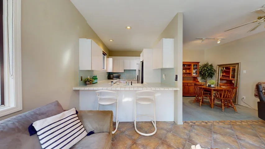 Kitchen with backsplash, white cabinets, tile countertops, a ceiling fan, and a peninsula
