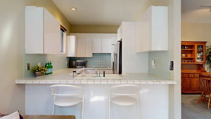 Kitchen featuring tile countertops, white cabinets, a kitchen breakfast bar, decorative backsplash, and appliances with stainless steel finishes