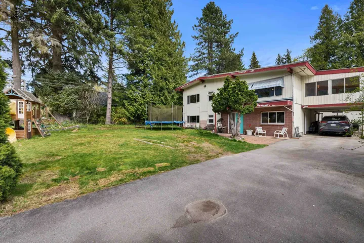 View of front of property featuring a front lawn, a trampoline, driveway, brick siding, and a carport