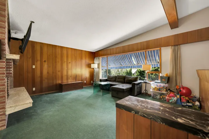 Living room with dark colored carpet, wooden walls, and beamed ceiling