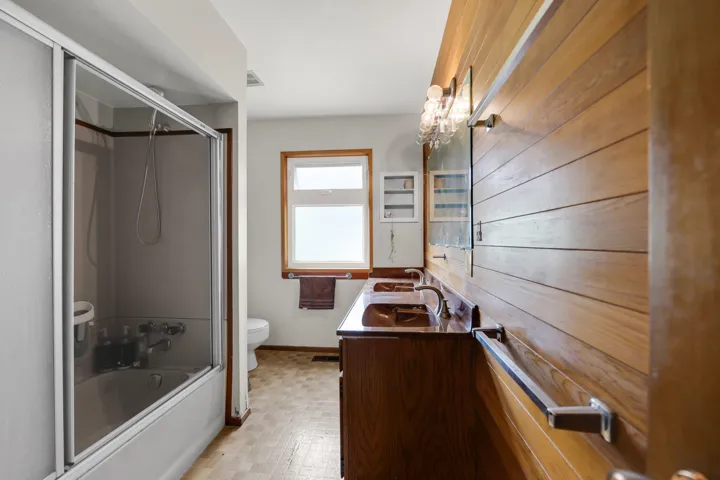 Full bath featuring double vanity, enclosed tub / shower combo, and light flooring