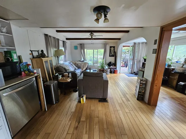 Living room with arched walkways, light wood-style floors, and beamed ceiling