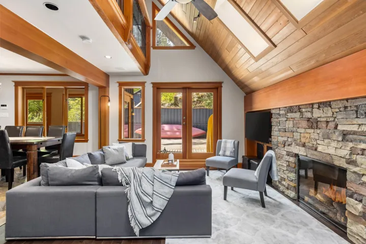 Living area with a fireplace, high vaulted ceiling, a skylight, wood finished floors, and a ceiling fan