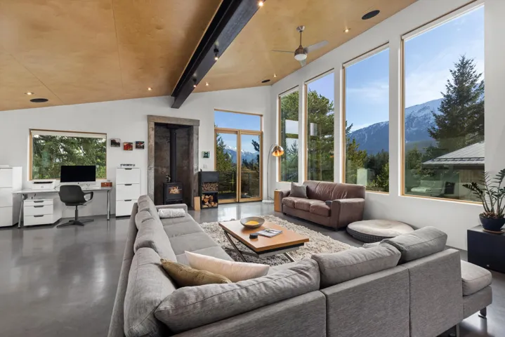 Living room with a wood stove, a desk, a mountain view, finished concrete floors, and vaulted ceiling with beams