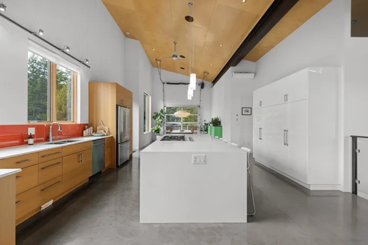 Kitchen featuring finished concrete flooring, modern cabinets, hanging light fixtures, a kitchen island with sink, and a ceiling fan