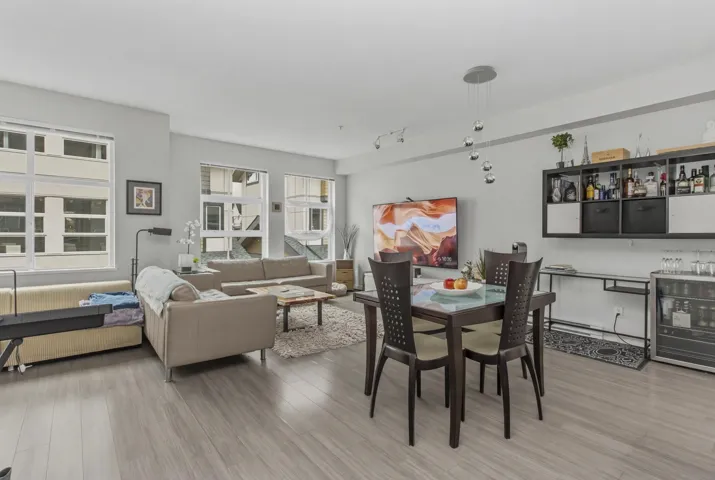 Open-concept living area with light-toned wood-finish flooring, multiple large windows, and a modern dining table