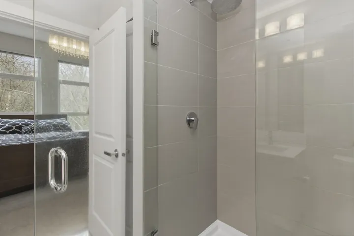 Glass-enclosed shower featuring large format wall tiles and a rainfall showerhead