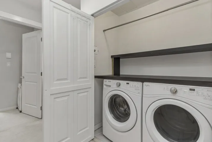 Dedicated laundry area featuring front-loading appliances, dark wood-finish countertop, coordinating open shelving, and a hanging rod