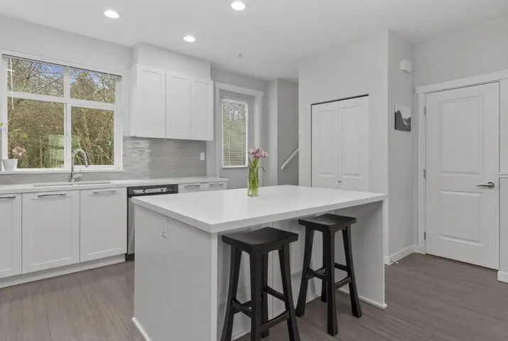 Modern kitchen featuring a central island with countertop seating, white shaker cabinetry, light-toned countertops, and a gray subway tile backsplash