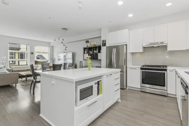 Kitchen featuring a large central island with an integrated microwave, white shaker cabinetry, stainless steel appliances, and a tiled backsplash