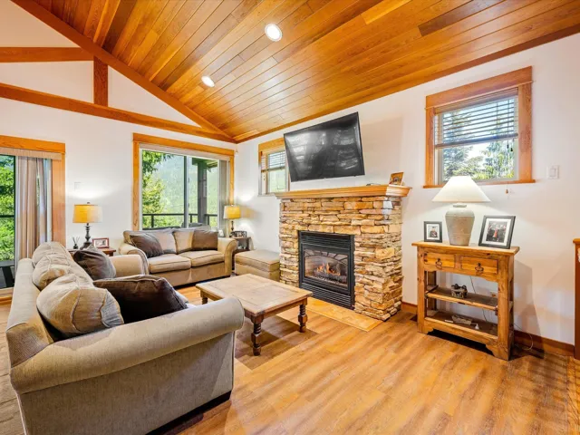 Living area featuring wooden ceiling, light wood-style flooring, a fireplace, vaulted ceiling, and baseboards