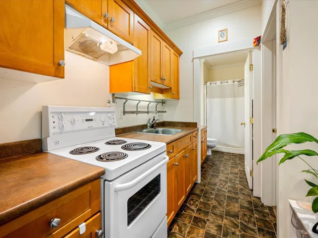 Kitchen featuring white electric range, under cabinet range hood, ornamental molding, a sink, and brown cabinetry