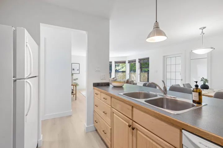 Kitchen featuring light brown cabinets, white appliances, dark countertops, and light wood-style floors