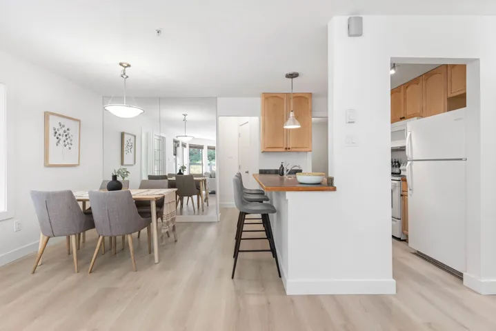 Kitchen with white appliances, a kitchen breakfast bar, light wood-style flooring, hanging light fixtures, and dark countertops