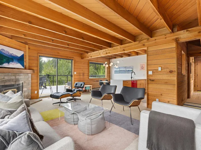 Carpeted living area with wooden walls, a fireplace with raised hearth, and a wooden ceiling with exposed beams