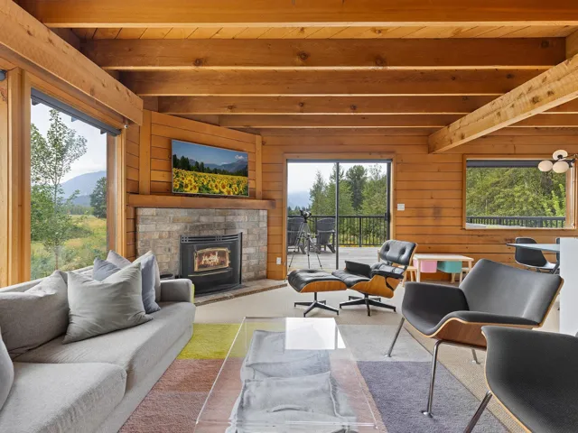 Living area with wooden walls, carpet, an outdoor brick fireplace, and a wood ceiling with exposed beams