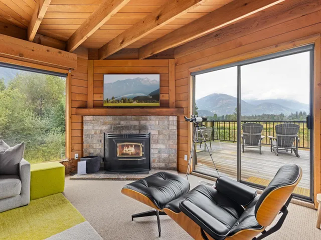 Living area featuring a mountain view, wooden walls, a brick fireplace, carpet floors, and a wooden ceiling with exposed beams