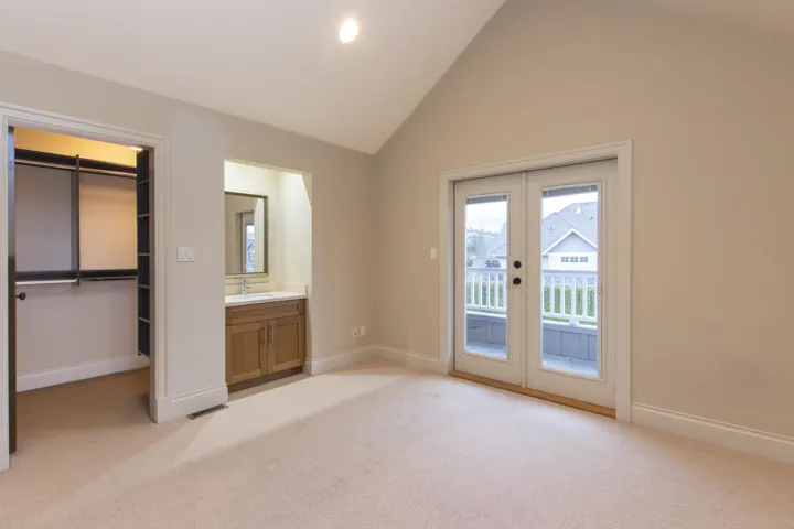 Unfurnished bedroom featuring lofted ceiling, light carpet, a spacious closet, access to exterior, and french doors