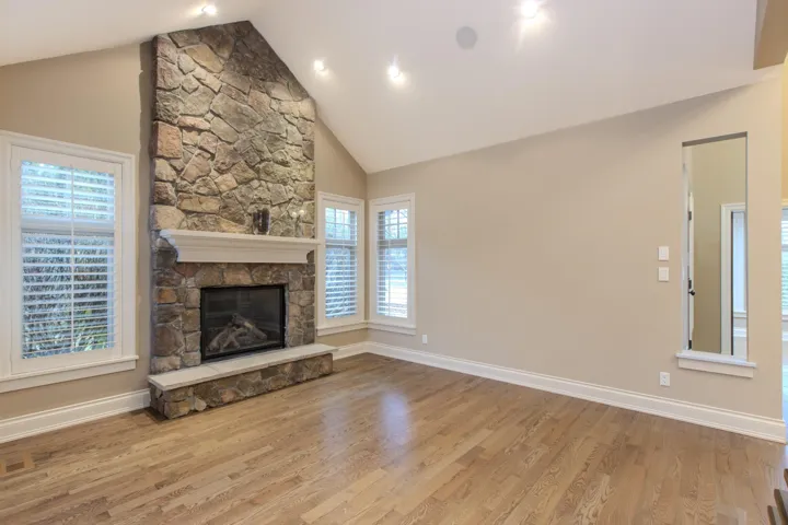 Unfurnished living room featuring a stone fireplace, light wood-type flooring, plenty of natural light, and high vaulted ceiling