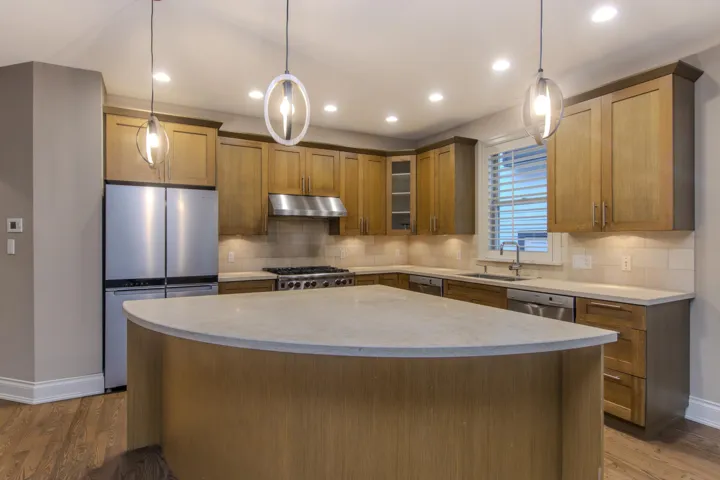 Kitchen featuring glass insert cabinets, tasteful backsplash, appliances with stainless steel finishes, hanging light fixtures, and brown cabinets