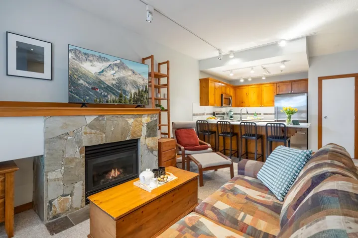 Open-concept living area featuring a stone-clad fireplace with a wood mantle