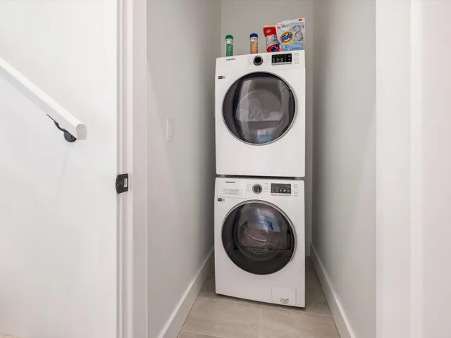 Clothes washing area with light tile patterned floors, laundry area, baseboards, and stacked washer and dryer