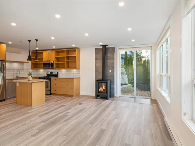 Kitchen with a wood stove, appliances with stainless steel finishes, a baseboard radiator, a kitchen island, and light wood-style floors