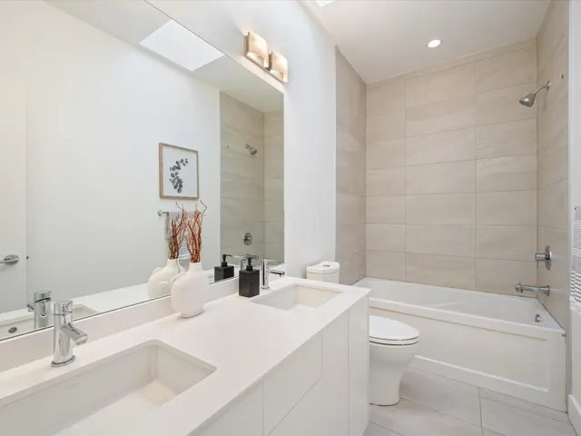 Bathroom with double vanity, a skylight, shower / bath combination, and light tile patterned flooring