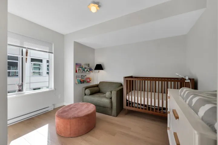 Bedroom with baseboard heating, light wood-type flooring, and a nursery area
