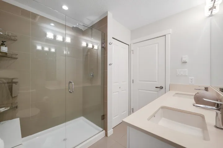 Full bathroom with double vanity, a textured ceiling, a stall shower, and light tile patterned flooring