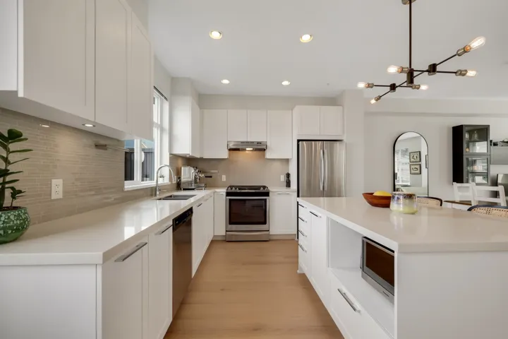 Kitchen with stainless steel appliances, a center island, white cabinets, hanging lights, and light wood-style flooring