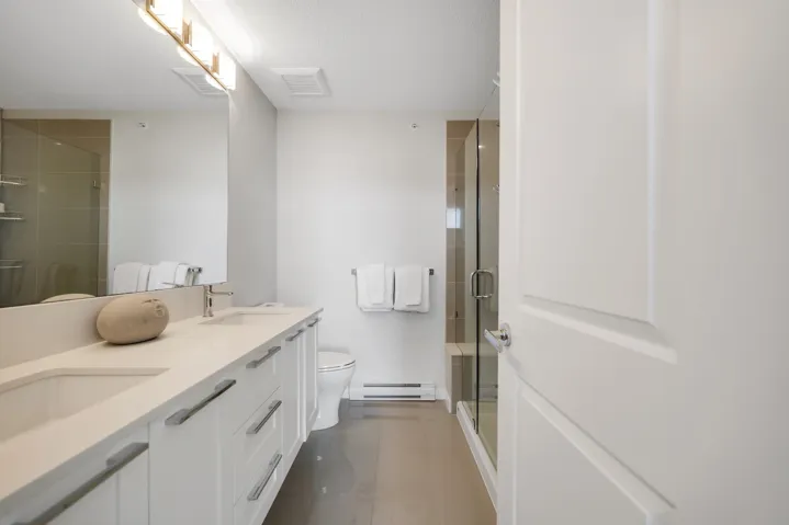 Bathroom with double vanity, a stall shower, a baseboard heating unit, and a textured ceiling