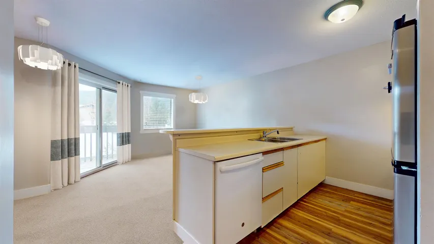 Kitchen featuring a peninsula, freestanding refrigerator, white dishwasher, hanging light fixtures, and a sink