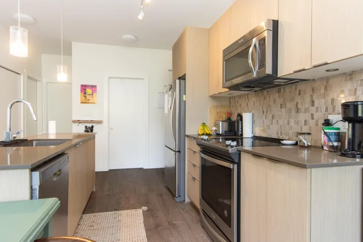 Kitchen featuring light brown cabinets, tasteful backsplash, a sink, stainless steel appliances, and dark wood-type flooring
