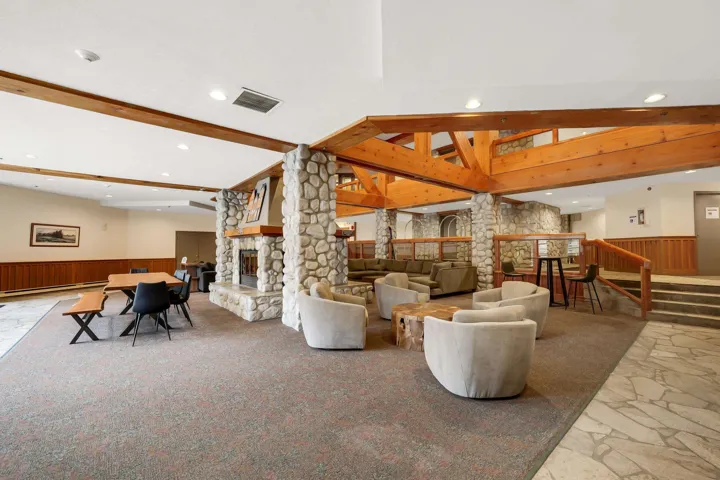 Living area featuring wainscoting, wooden walls, a stone fireplace, decorative columns, and lofted ceiling with beams