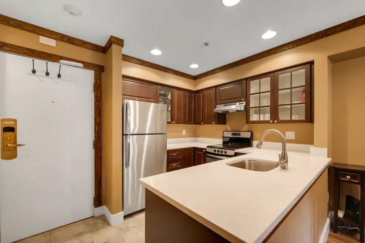 Kitchen featuring glass insert cabinets, stainless steel appliances, a peninsula, recessed lighting, and light stone counters