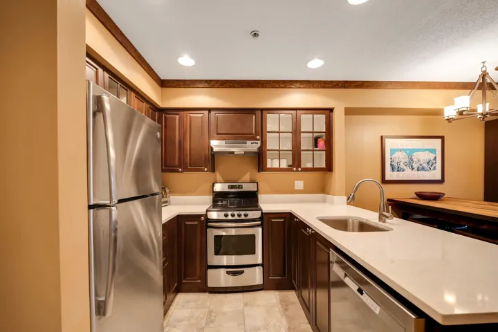 Kitchen featuring glass fronted cabinets, stainless steel appliances, a peninsula, light stone countertops, and hanging lights