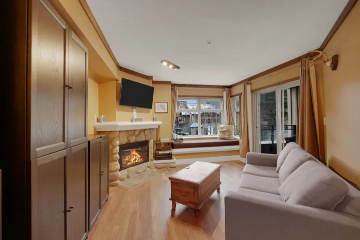 Living area with light wood-type flooring, ornamental molding, and a stone fireplace