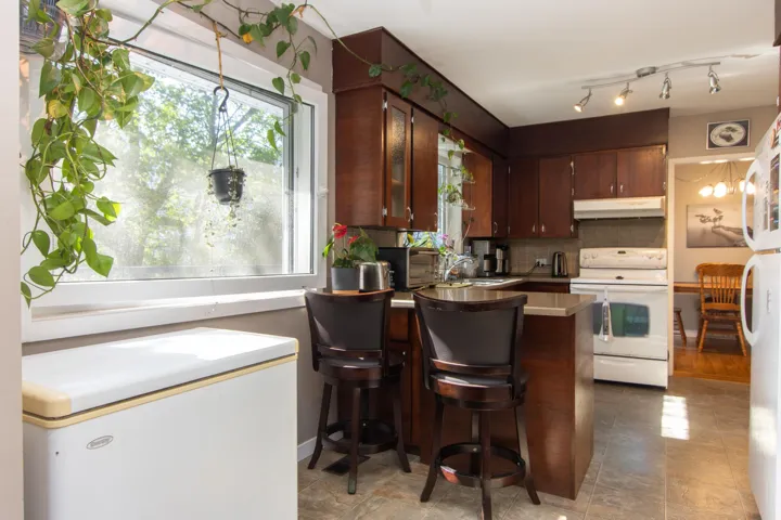 Kitchen with a peninsula, white appliances, under cabinet range hood, light countertops, and tasteful backsplash