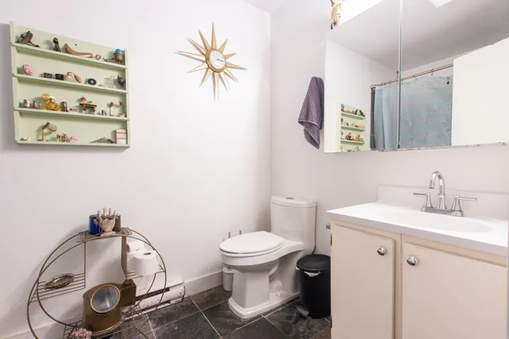 Bathroom featuring toilet, a shower with curtain, stone finish floor, baseboards, and vanity