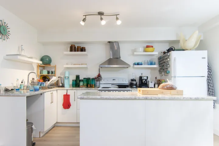Kitchen with white appliances, open shelves, light wood-type flooring, wall chimney exhaust hood, and a center island