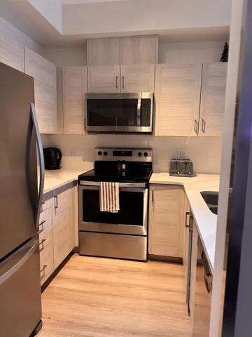 Kitchen with light countertops, light wood-type flooring, appliances with stainless steel finishes, and backsplash
