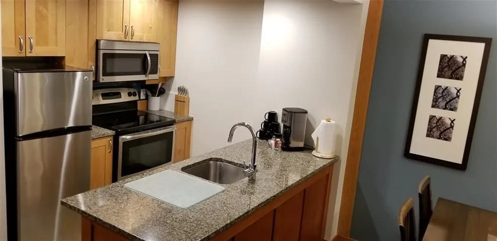 Kitchen featuring dark stone countertops, appliances with stainless steel finishes, and light brown cabinets